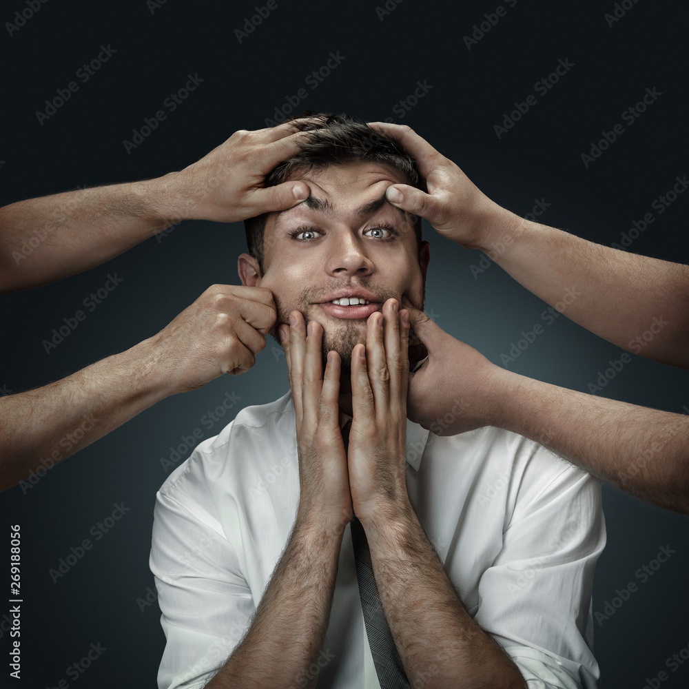 Fototapeta premium A male model surrounded by hands like his own thoughts on dark background. A young man doubts, can't choose the right decision and decide. Concept of mental problems, troubles in work, indecision.