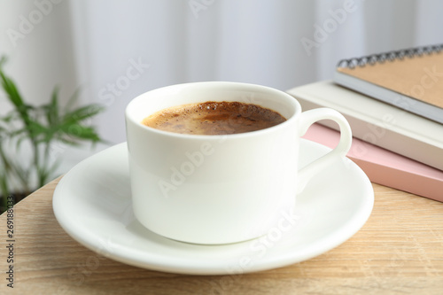 Cup of coffee and notebooks on wooden table against light background with plant  space for text and closeup