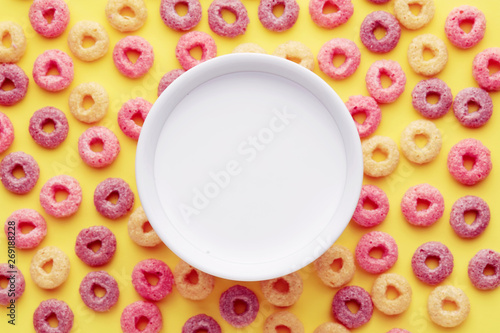 Bowl of milk on colorful corn flakes cereal ring loops. Overhead close up view.