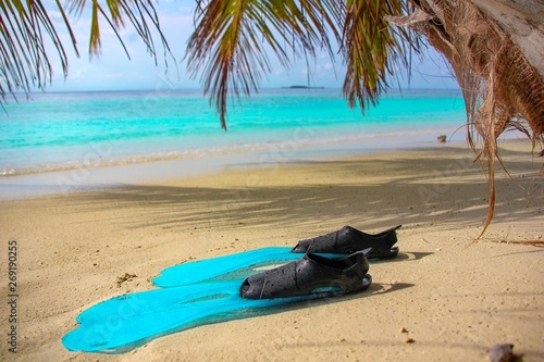 Blue flippers lie on the shore of a tropical island with white sand in blue lagoon, Indian Ocean, Maldives