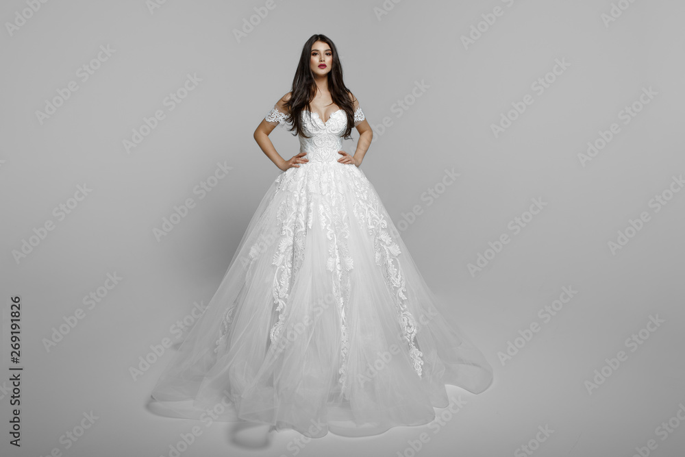 Luxury bride in long white wedding princess dress. Charming bride in a magnificent wedding dress. Bride in luxurious suites. Female models poses standing with hands on her waist