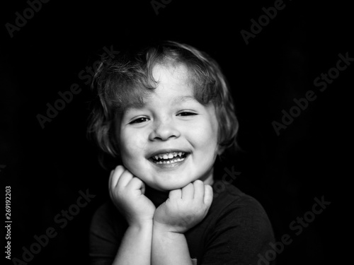 Portrait of a little smiling  curly-haired cute boy on a dark background