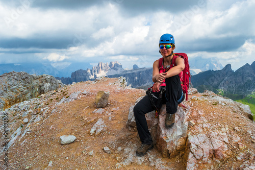 Female climber on Averau peak at the end of a via ferrata route, with dark storm clouds approaching in the background, in the Dolomite mountains, Italy. Tourism in Europe in the summer.