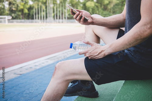 Young fitness athlete man resting on bench with bottle of water preparing to running on road track, exercise workout wellness concept
