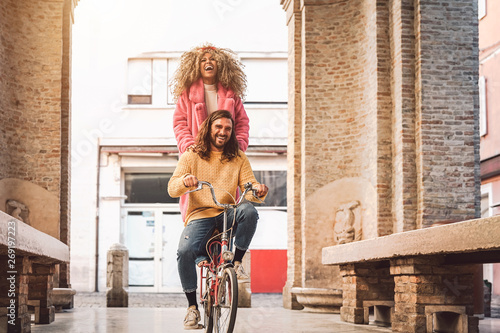 Happy couple going on bicycle in the city center - Young people having fun outdoor - Millennial generation and youth lifestyle concept