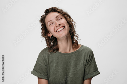 Emotional curly woman smiling widely  closing her eyes