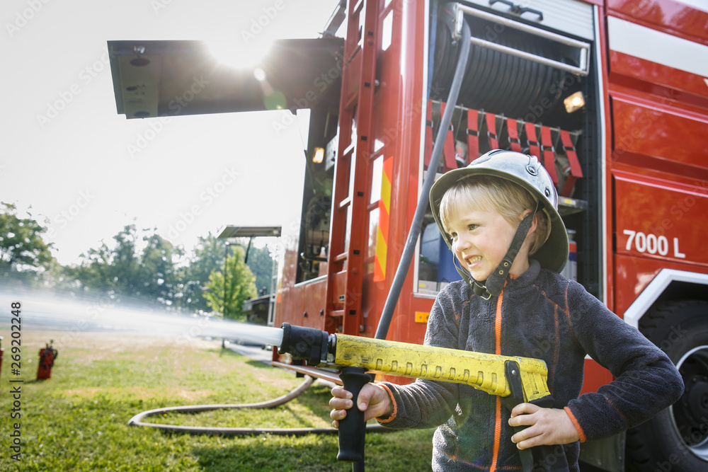 Little fireman holding firehose nozzle and splashing water.