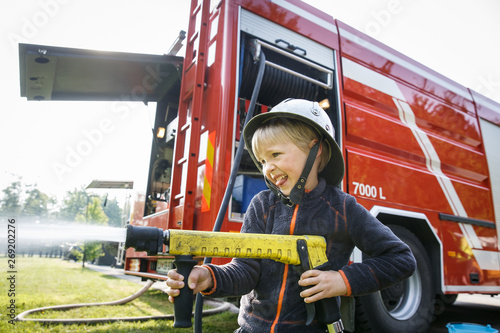Little fireman holding firehose nozzle and splashing water.