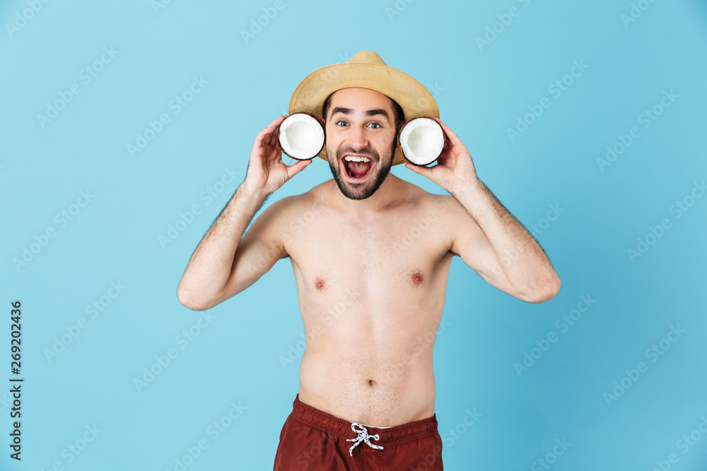 Photo of beautiful shirtless tourist man wearing straw hat smiling while holding two coconut parts