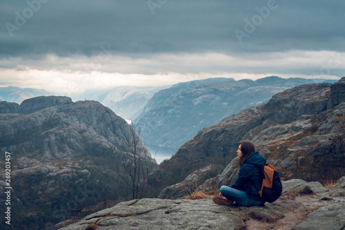 Woman sitting on the edge of the cliff and admiring beautiful landscape of rocky mountains and fjord in Preikestolen, Stavanger, Norway. Top view