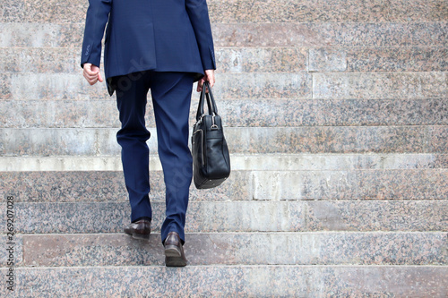 Man in a business suit with briefcase climbing steep stairs, male legs in motion on the steps. Concept of career, success, moving to the top, official or businessman