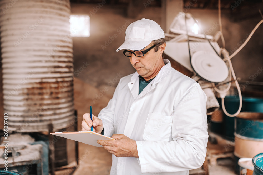 Serious Caucasian veterinarian in white uniform writing down results of animal examination while standing in front of barn. Serious Caucasian veterinarian in white uniform writing down results of animal examination while standing in front of barn.