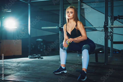 Young attracrive sport woman sitting with water bottle on crossfit gym background © Aleksander