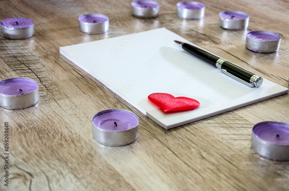 Notepad with pen and red heart on wooden background. Side view.