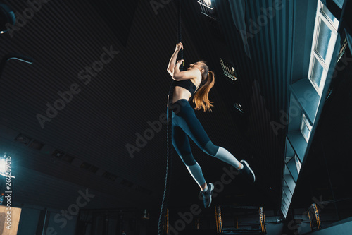 Full length wide angle shot of a woman performing rope climbs at the gym. Copyspace background with athletics healthy composition. Crossfit and fitness