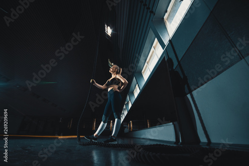 Full length wide angle shot of a woman performing rope climbs at the gym. Copyspace background with athletics healthy composition. Crossfit and fitness