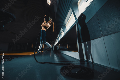 Full length wide angle shot of a woman performing rope climbs at the gym. Copyspace background with athletics healthy composition. Crossfit and fitness