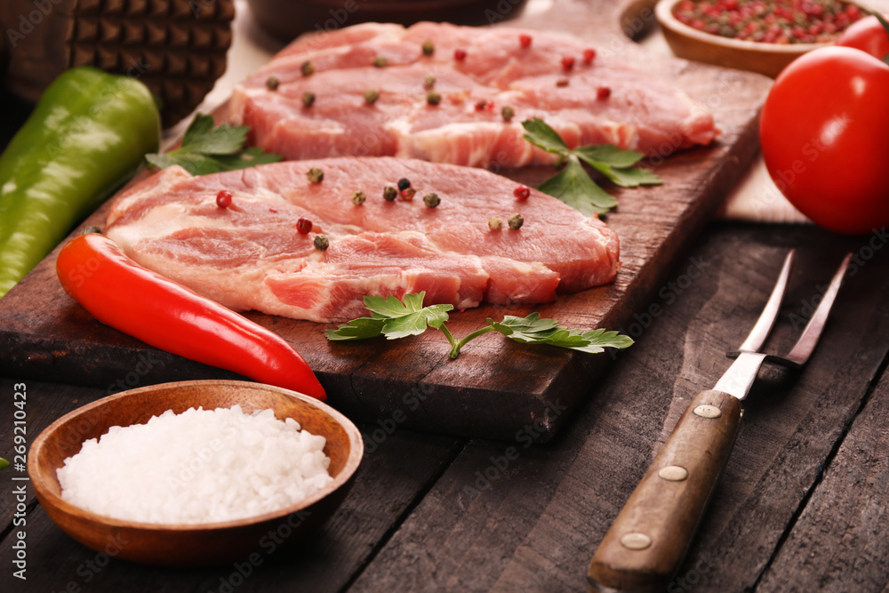 Raw meat. Raw pork steak on a cutting board with vegetables, peppers, tomato, salt and spices on a black background Raw meat. Raw pork steak on a cutting board with vegetables, peppers, tomato, salt and spices on a black background