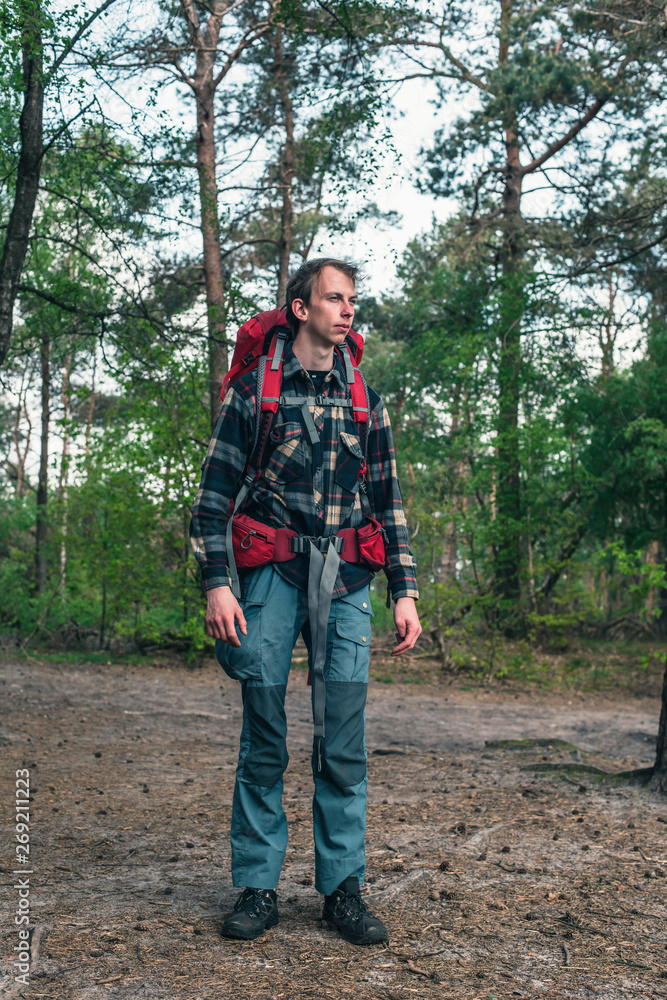 Young man with red backpack in forest in spring.