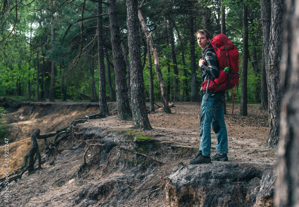 Naklejka premium Young man with red backpack at edge of canyon in spring forest.