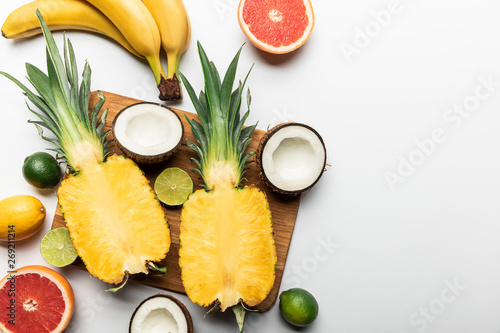 Fototapeta Naklejka Na Ścianę i Meble -  top view of cut and whole exotic fruits on wooden chopping board on white background