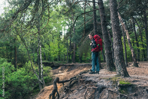 Young man with red backpack at edge of canyon in spring forest.