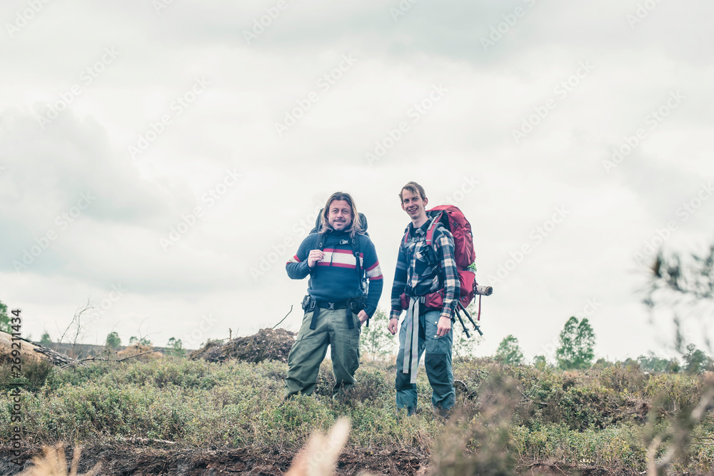 Two happy backpackers standing in wilderness under cloudy sky.