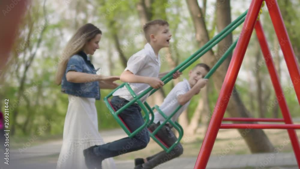 Happy mother pushing laughing two sons on swing in a park. Outdoor recreation. Happy mother pushing laughing two sons on swing in a park. Outdoor recreation.