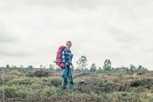 Smiling backpacker standing in wilderness under cloudy sky.
