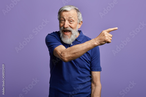 cheerful man pointing at copy space and looking at the camera. close up portrait, place for advert. happy old man indicating somewhere