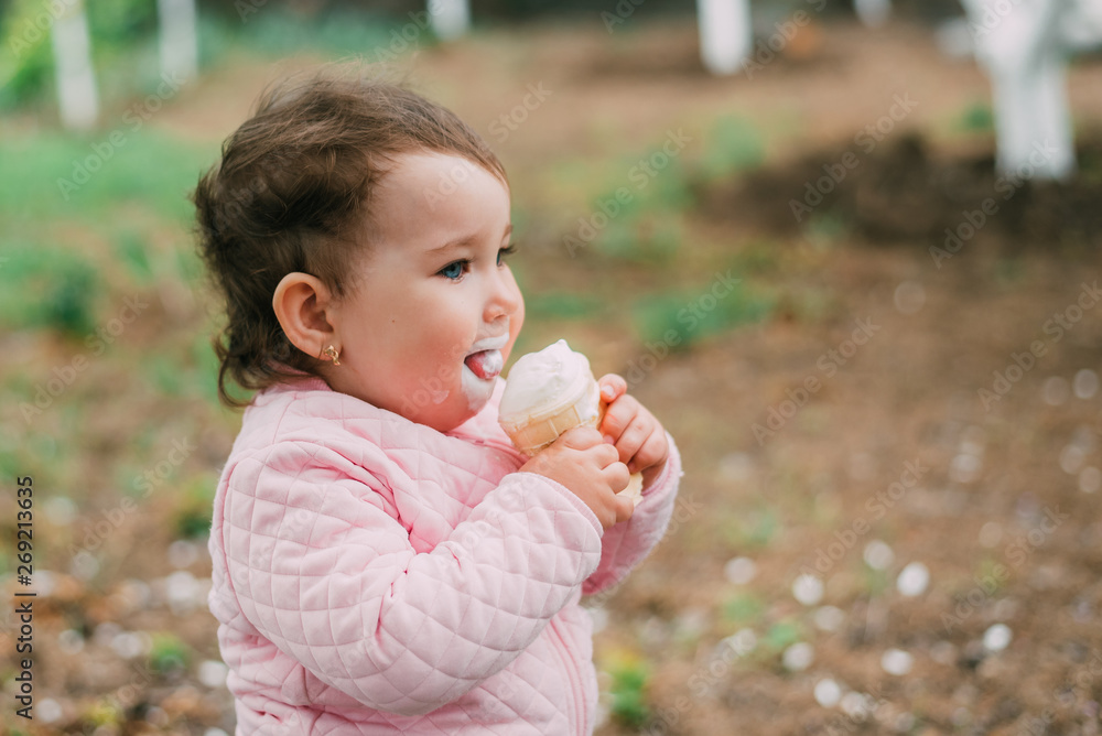little girl in the garden on the background of greenery and trees very cute eating ice cream in a waffle Cup little girl in the garden on the background of greenery and trees very cute eating ice cream in a waffle Cup