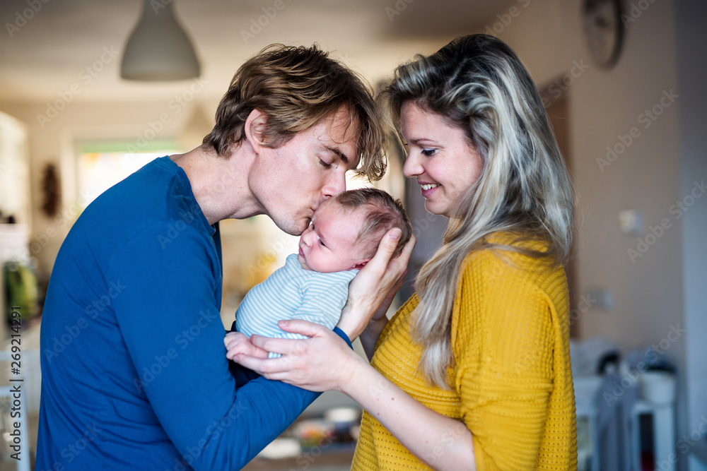 Fototapeta premium Beautiful young parents with a newborn baby at home, kissing.
