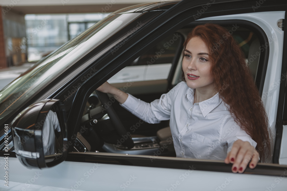 Beautiful young businesswoman getting in a new car, while shopping for new auto at the dealership. Attractive female cusotmer examining cars for sale. Beautiful woman choosing new automobile to buy