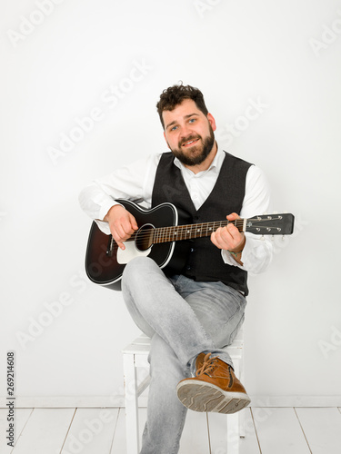 man with black hair and beard playing and singing with acoustic guitar on white background and is happy photo