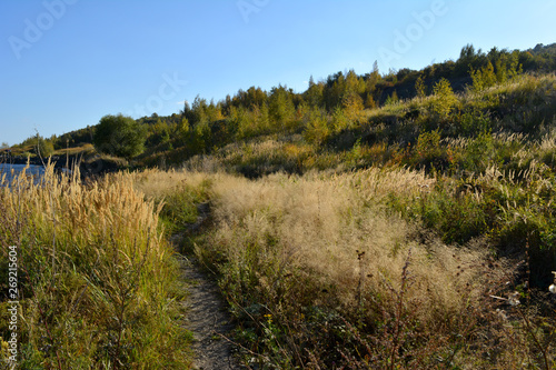 Path through meadow with dry herbs to the hills on river bank. Nature in the beginning of autumn.