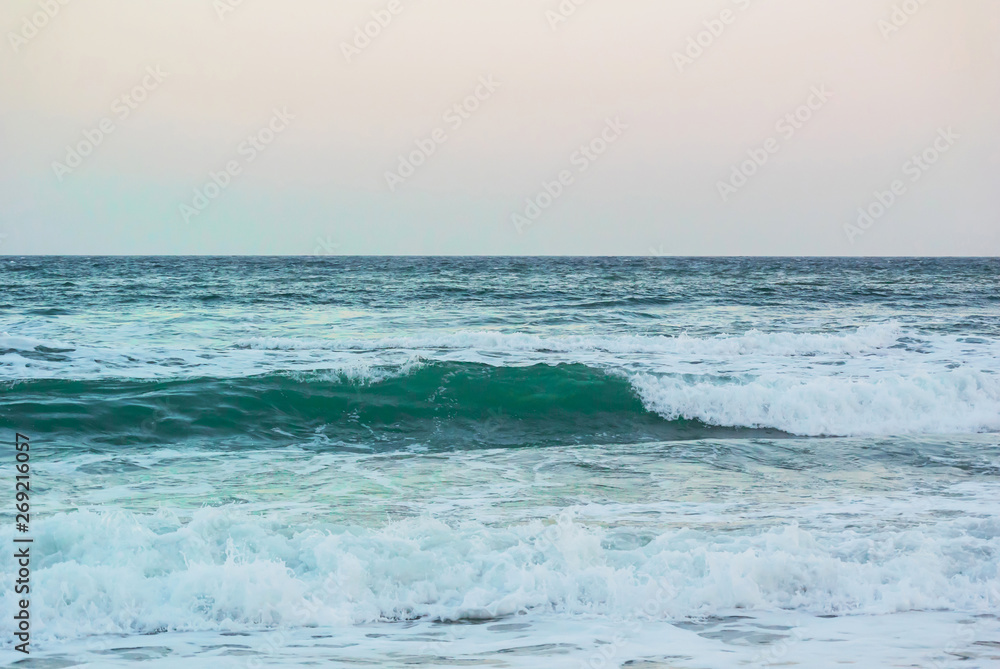 Photo of sea waves with sea foam at sunset of the day, against the backdrop of a clear evening sky