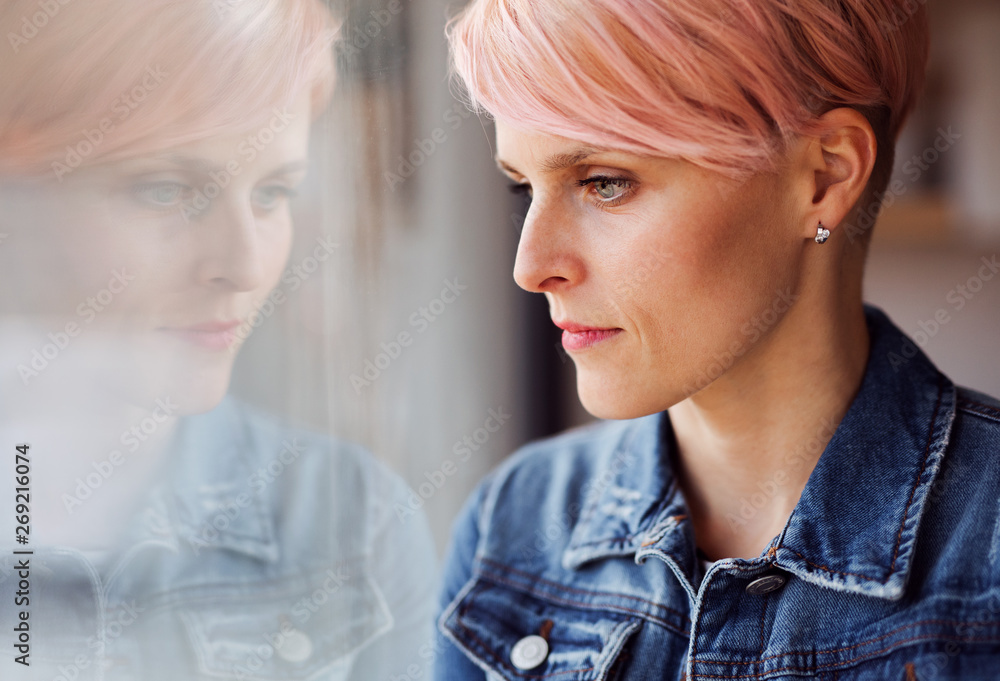 A close-up portrait of young attractive woman standing by window at home. A close-up portrait of young attractive woman standing by window at home.