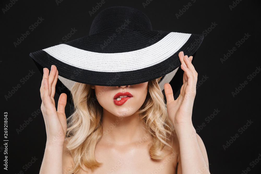 Blonde woman with bright makeup red lips posing isolated over black wall background wearing hat. Blonde woman with bright makeup red lips posing isolated over black wall background wearing hat.