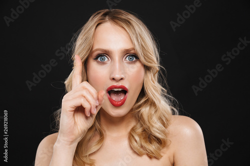 Shocked young blonde woman with bright makeup red lips posing isolated over black wall background.