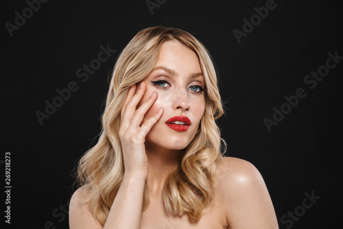 Pretty young blonde woman with bright makeup red lips posing isolated over black wall background.