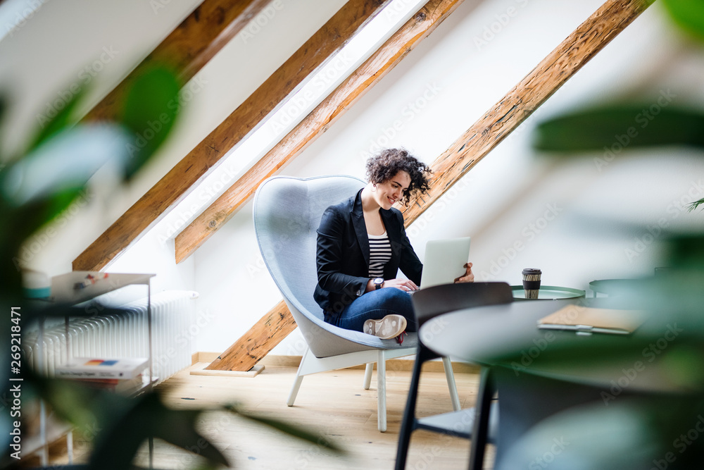 Fototapeta premium Young businesswoman with laptop sitting at the table in office, working.
