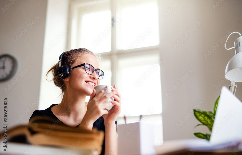 A young female student sitting at the table, using headphones when studying. A young female student sitting at the table, using headphones when studying.