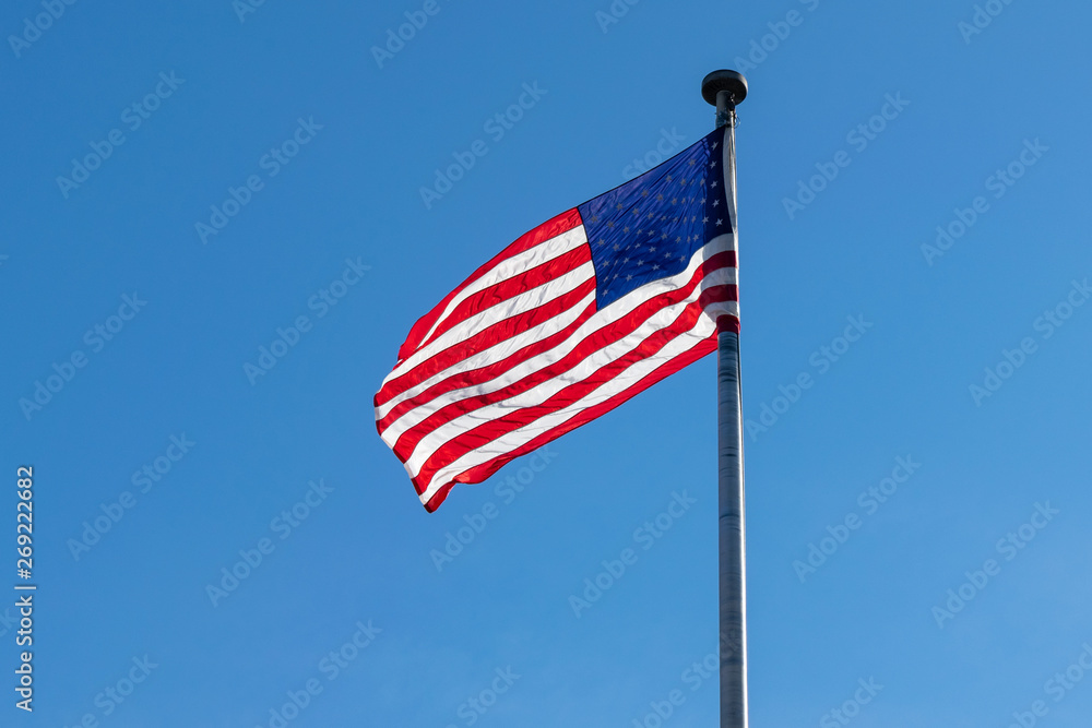 American flag, Stars & Stripes, waving in the wind, against a beautiful blue sky on a sunny summer day American flag, Stars & Stripes, waving in the wind, against a beautiful blue sky on a sunny summer day