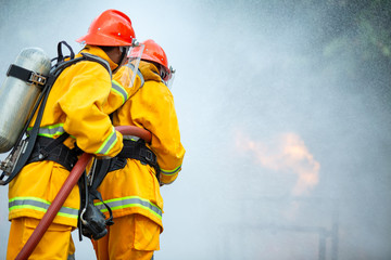 Firefighters spraying high pressure water to fire with copy space, Big bonfire in training, Firefighter wearing a fire suit for safety under the danger case.
