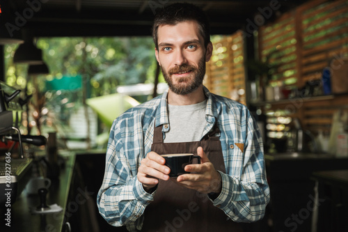 Image of kind barista man making coffee while working in cafe or coffeehouse outdoor