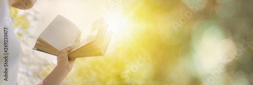 woman 's hand holding book opening for wisdom with sunshine as freedom of knowledge concept on green bokeh background, banner style