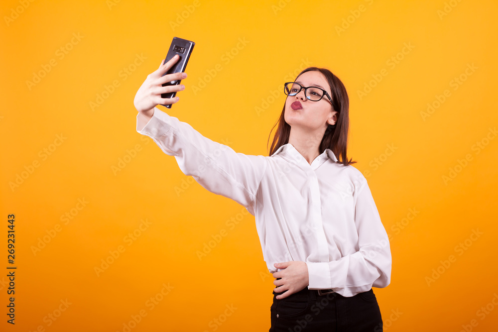 Pretty young girl making a selfie and doing duck lips to the camera in studio over yellow background Pretty young girl making a selfie and doing duck lips to the camera in studio over yellow background