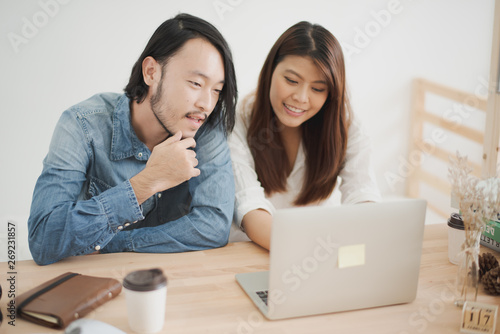 Young Asian man and woman are sitting and looking at laptop computer and smiling feeling happy in the bedroom at home. the couple are shopping online and considering. the life at home concept.