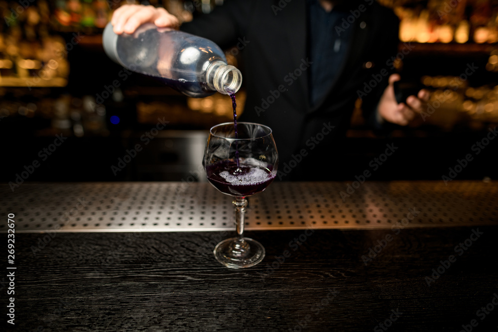 Bartender pours cocktail and adds liquor in glass