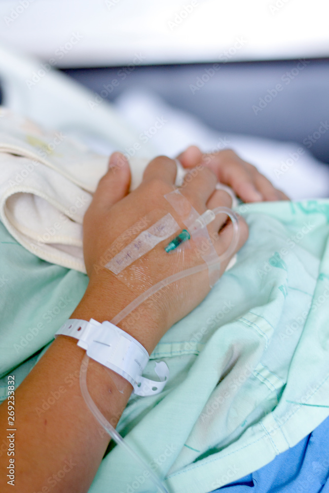 The saline solution of the patient's hand was lying in bed in a medical room. The saline solution of the patient's hand was lying in bed in a medical room.